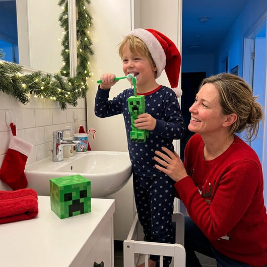 Boy in a Santa hat brushing his teeth with the Creeper Minecraft toothbrush, his mom smiling beside him